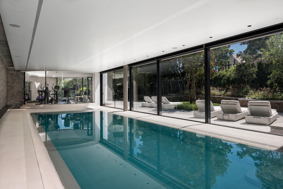 Expansive contemporary indoor rectangular swimming pool in Hampshire with natural stone paving.