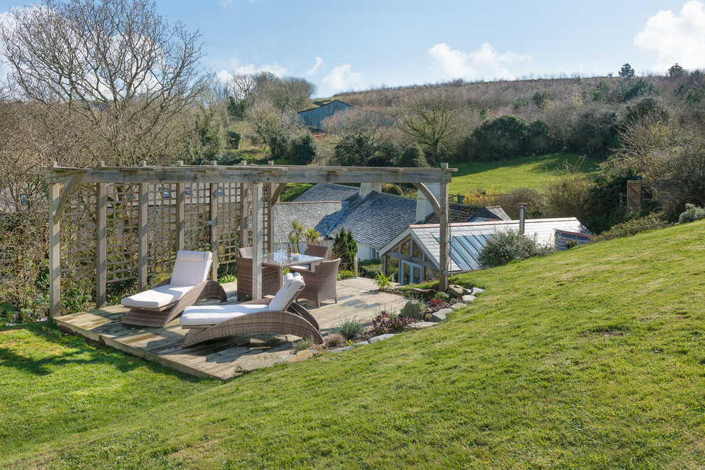 Mid-sized cottage backyard deck photo in Devon with a pergola