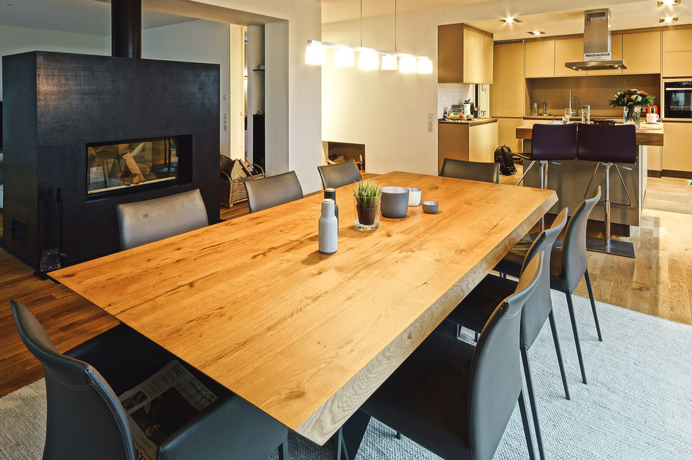Foto di una sala da pranzo minimal di medie dimensioni con pareti bianche, pavimento in legno massello medio, stufa a legna, cornice del camino in metallo e pavimento marrone