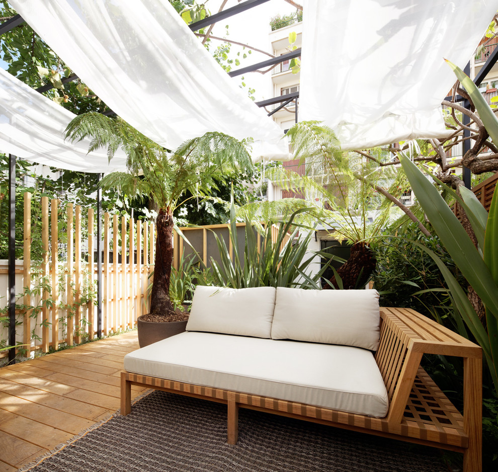Modelo de terraza tropical de tamaño medio en patio trasero con jardín de macetas y toldo