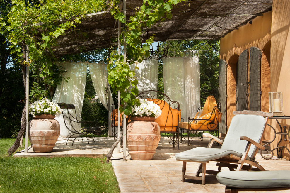 Imagen de patio mediterráneo en patio delantero con jardín de macetas, pérgola y adoquines de piedra natural