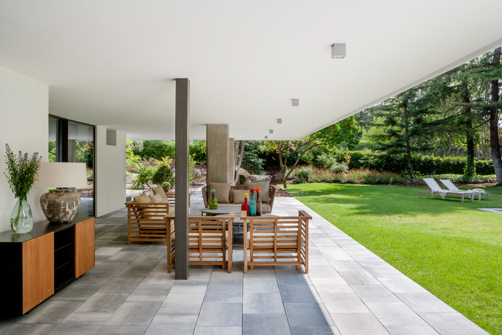Стильный дизайн: огромный двор на заднем дворе в современном стиле с мощением тротуарной плиткой и навесом - последний тренд
