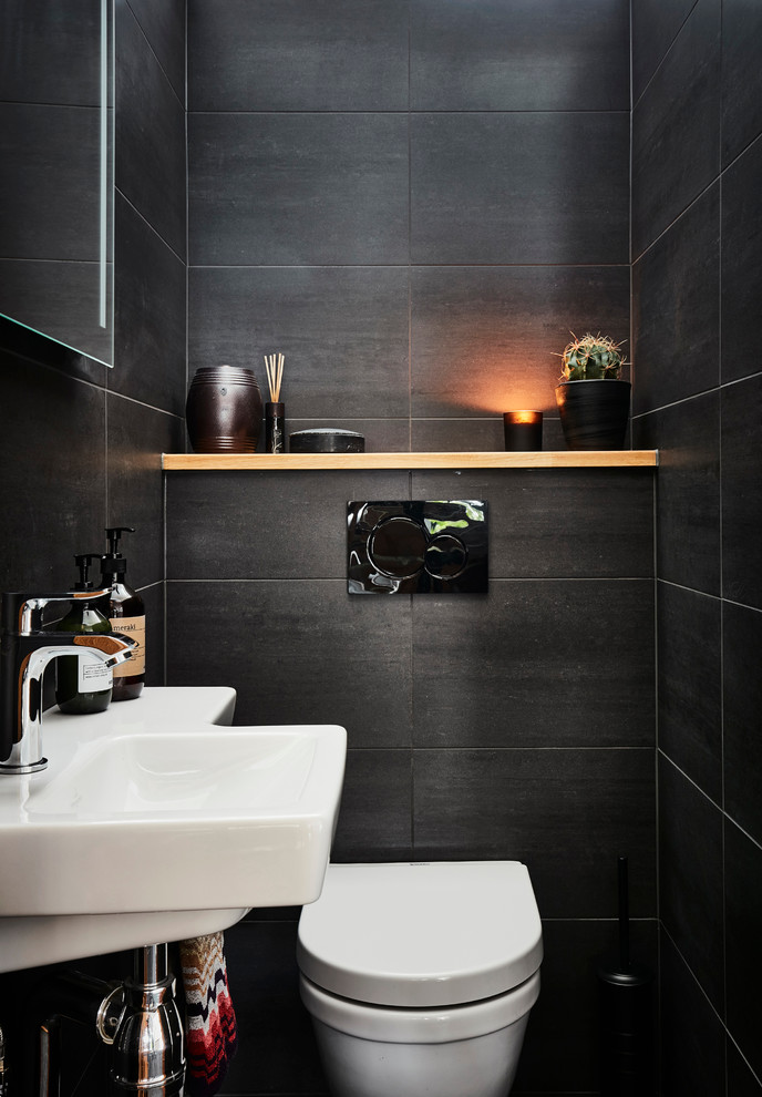 Cette image montre un WC et toilettes minimaliste de taille moyenne avec WC à poser, des carreaux de céramique, un mur noir, un placard à porte plane, des portes de placard blanches, un carrelage noir, un plan vasque et un sol noir.