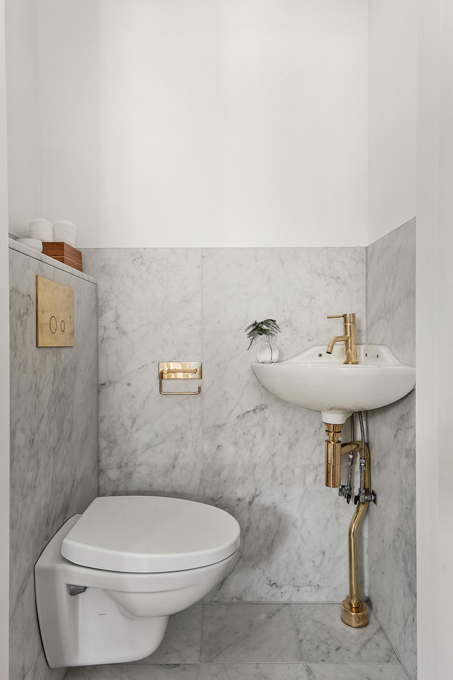Inspiration för stora nordiska toaletter, med en vägghängd toalettstol, vita väggar, marmorgolv och ett väggmonterat handfat