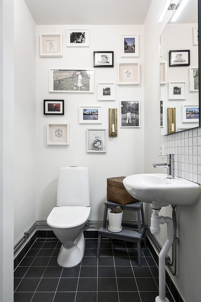 Foto på ett mellanstort nordiskt toalett, med en toalettstol med separat cisternkåpa, vita väggar, ett piedestal handfat, vit kakel, svart kakel, klinkergolv i keramik och svart golv