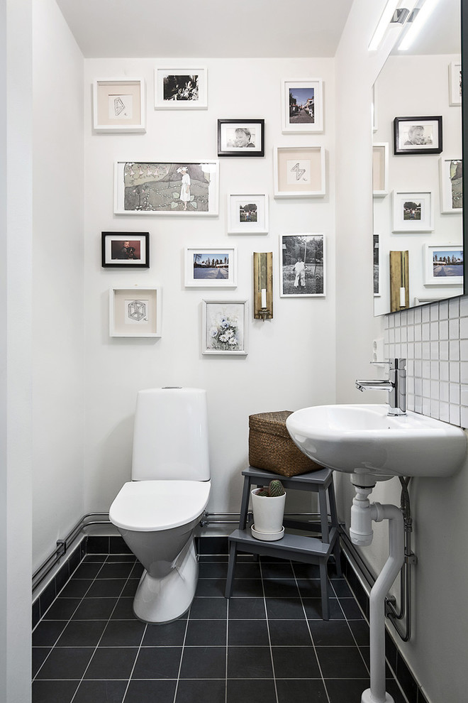 Diseño de aseo escandinavo, de tamaño medio, con sanitario de dos piezas, paredes blancas, lavabo con pedestal, baldosas y/o azulejos blancos, baldosas y/o azulejos negros, suelo de baldosas de cerámica y suelo negro