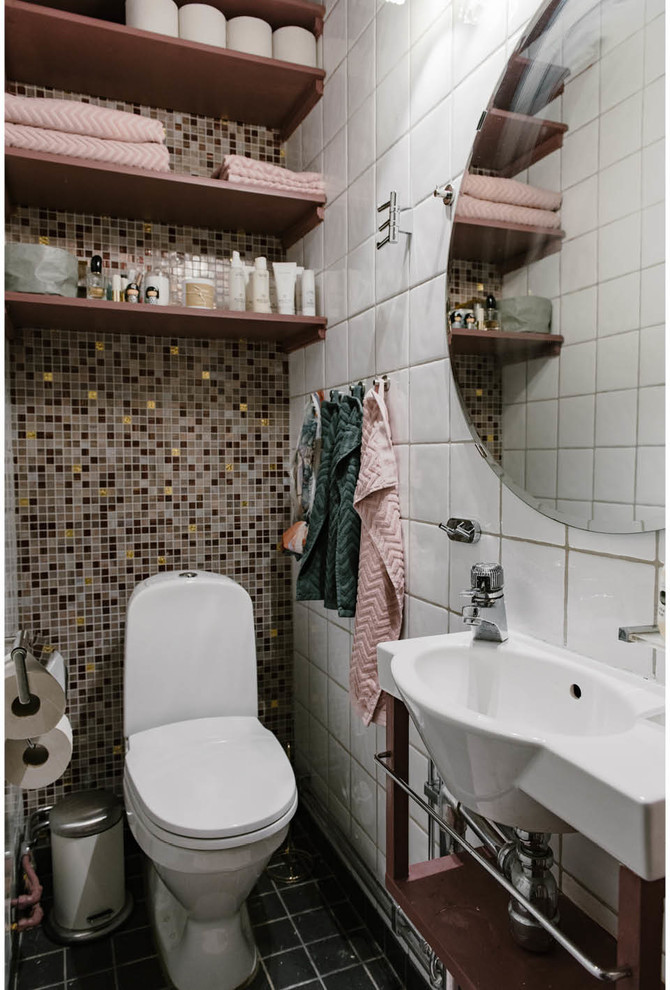 Exempel på ett litet skandinaviskt toalett, med öppna hyllor, en toalettstol med hel cisternkåpa, mosaik, ett väggmonterat handfat, svart golv, skåp i mörkt trä, flerfärgad kakel och vit kakel