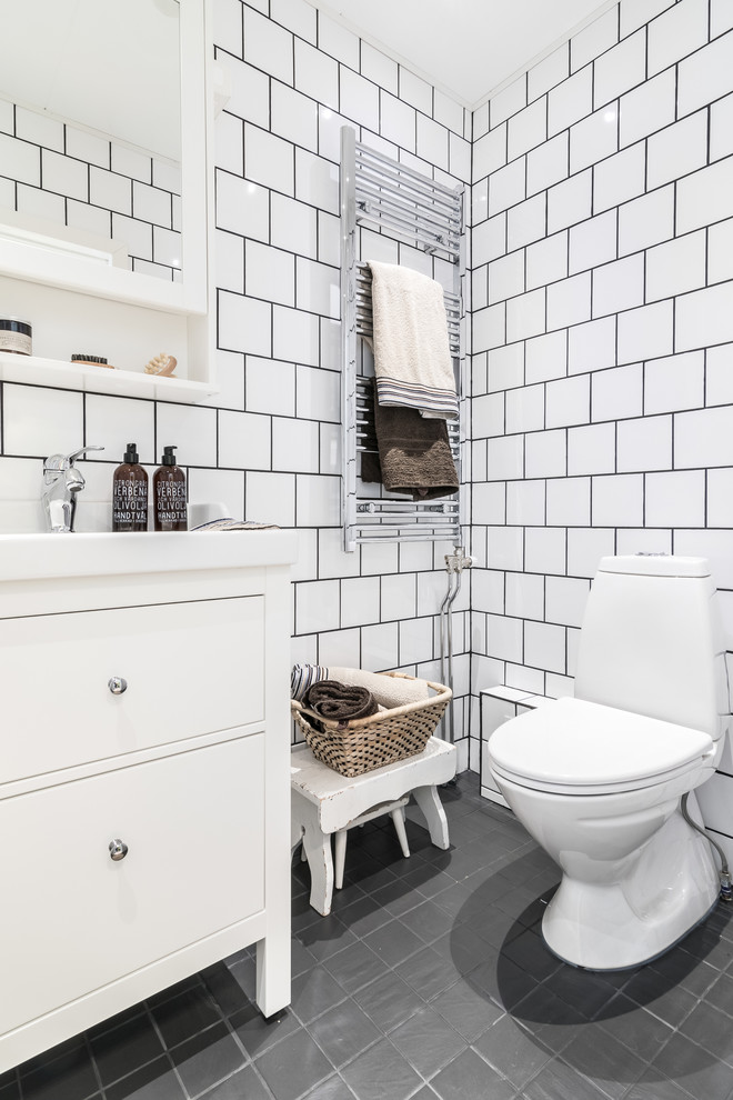 Skandinavisk inredning av ett mellanstort toalett, med släta luckor, vita skåp, en toalettstol med separat cisternkåpa, vit kakel, porslinskakel, vita väggar, ett integrerad handfat och grått golv