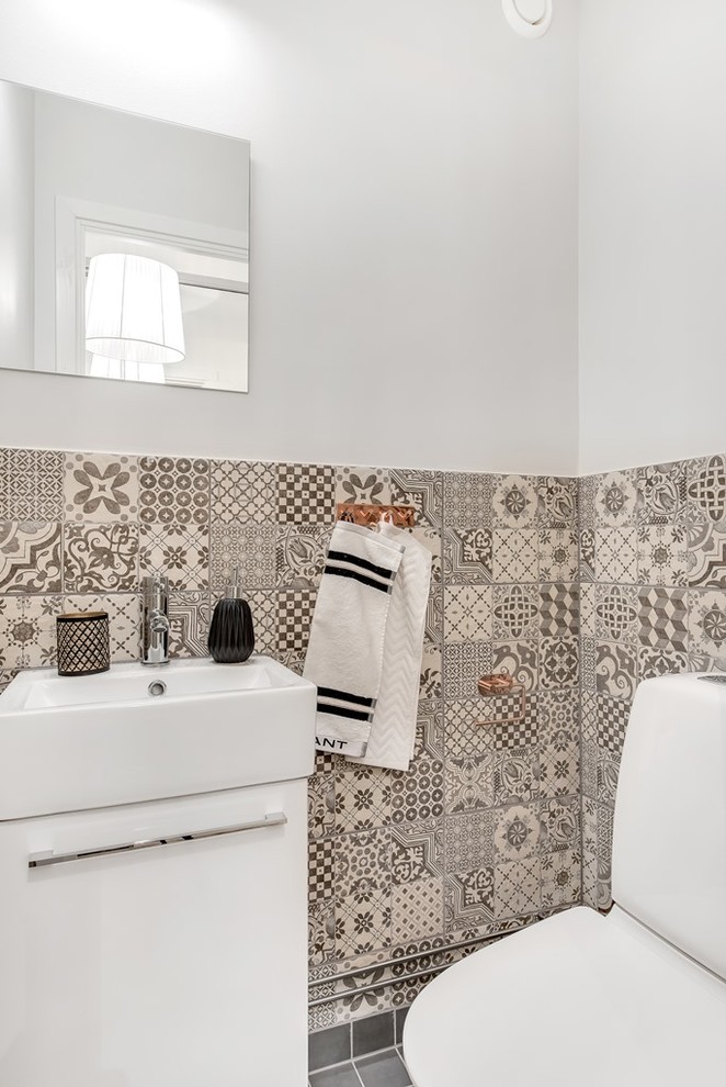 Foto på ett litet nordiskt toalett, med vita skåp, grå kakel, keramikplattor, grå väggar, klinkergolv i keramik och släta luckor