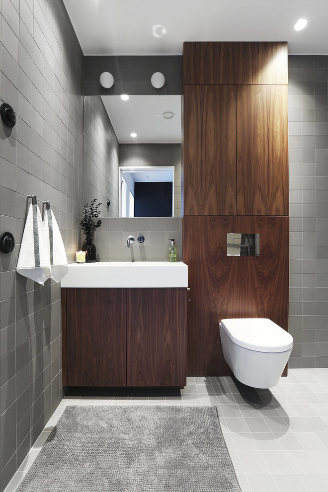 Inredning av ett modernt mellanstort toalett, med släta luckor, skåp i mörkt trä, en vägghängd toalettstol, grå kakel, grå väggar, ett integrerad handfat, keramikplattor, klinkergolv i keramik och grått golv
