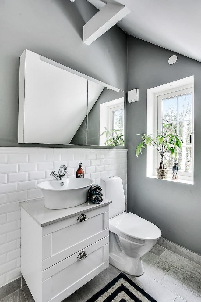 Idées déco pour un WC et toilettes scandinave avec un placard à porte shaker, des portes de placard blanches, un carrelage blanc, un carrelage métro, un mur gris, une vasque, un sol gris et un plan de toilette gris.