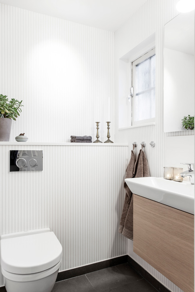 Nordisk inredning av ett litet toalett, med släta luckor, skåp i ljust trä, vita väggar, ett avlångt handfat och svart golv