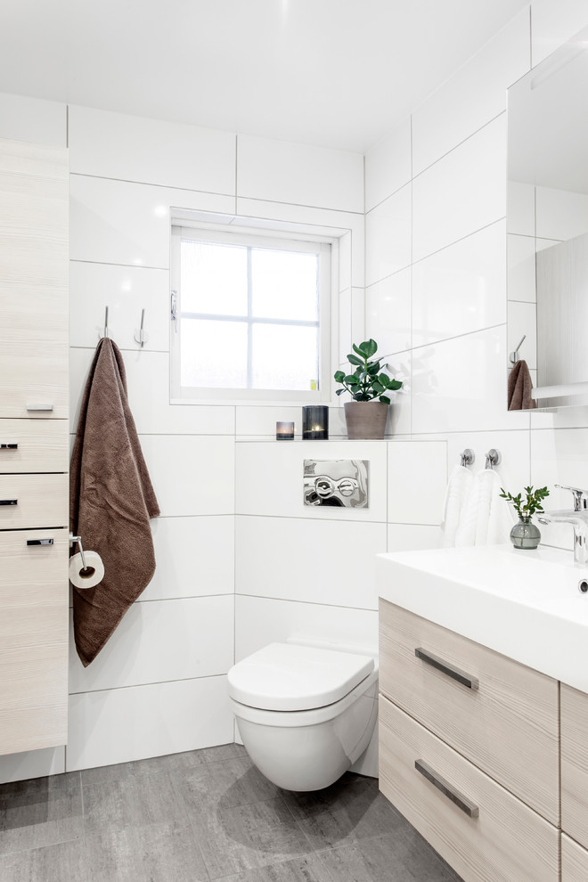 На фото: большой туалет в скандинавском стиле с плоскими фасадами, светлыми деревянными фасадами, унитазом-моноблоком, белой плиткой, керамогранитной плиткой, белыми стенами, полом из известняка, накладной раковиной и серым полом с