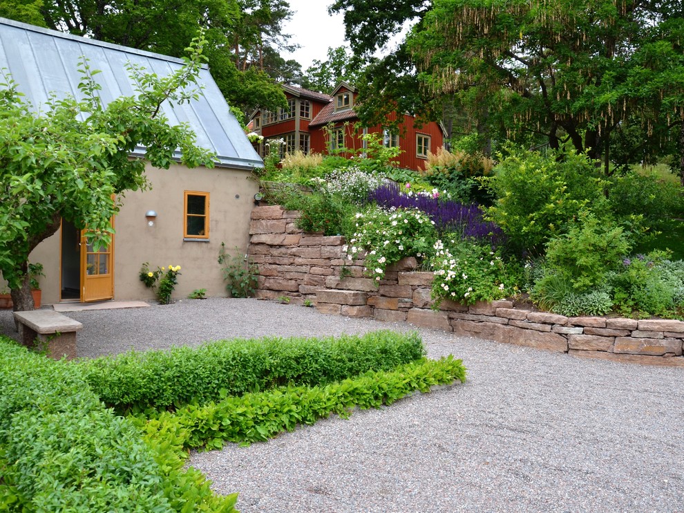 Nordisk inredning av en mellanstor formell trädgård framför huset, med grus på sommaren
