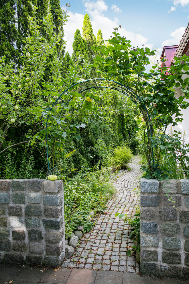 Imagen de jardín tradicional de tamaño medio en verano en patio delantero con jardín francés, muro de contención y adoquines de piedra natural