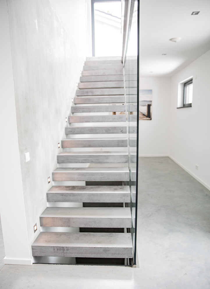 Immagine di una scala a rampa dritta minimalista di medie dimensioni con pedata in cemento, nessuna alzata e parapetto in vetro