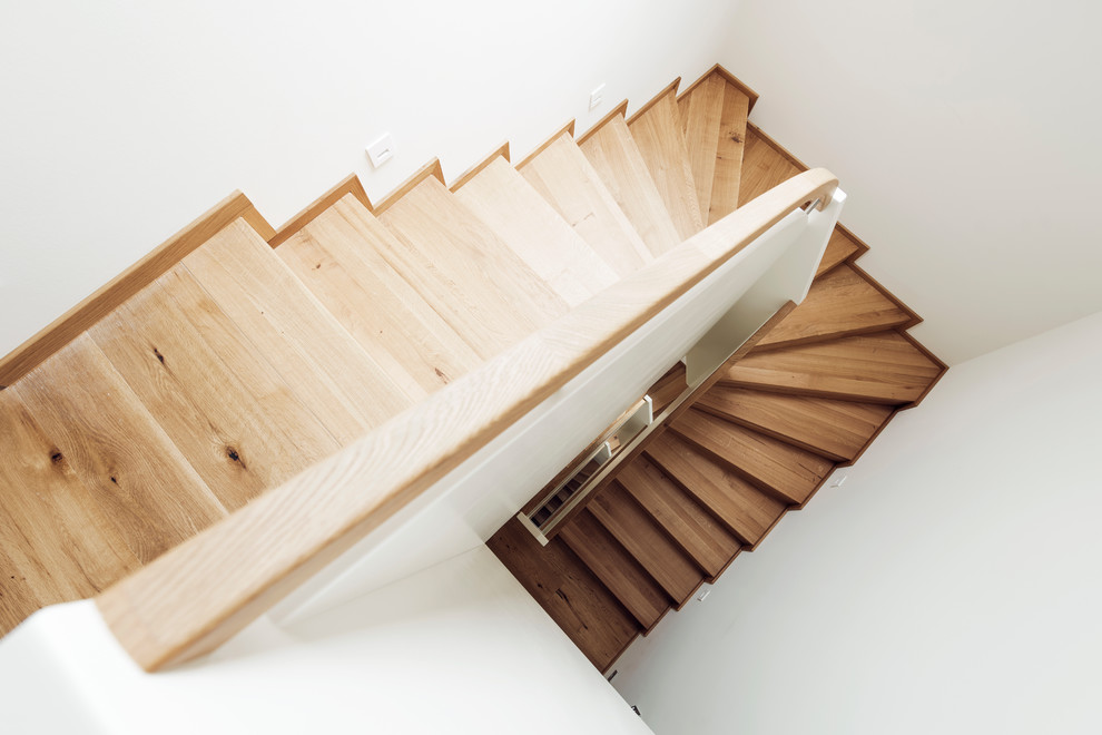 Свежая идея для дизайна: изогнутая деревянная лестница среднего размера в современном стиле с деревянными ступенями и перилами из смешанных материалов - отличное фото интерьера
