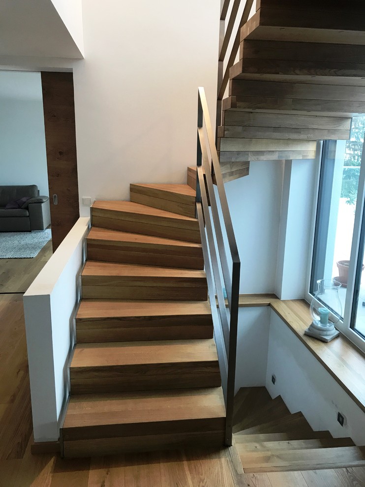 Imagen de escalera curva actual grande con escalones de madera, contrahuellas de madera y barandilla de metal