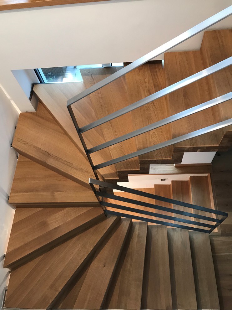 Réalisation d'un grand escalier courbe design avec des marches en bois, des contremarches en bois et un garde-corps en métal.