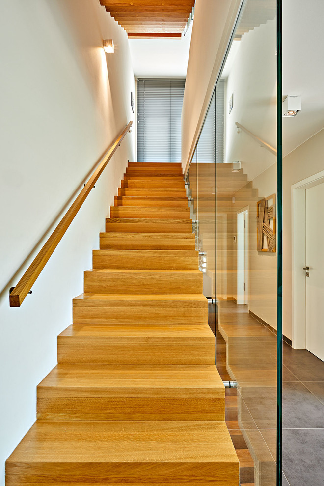 Diseño de escalera recta actual grande con escalones de madera, contrahuellas de madera y barandilla de vidrio
