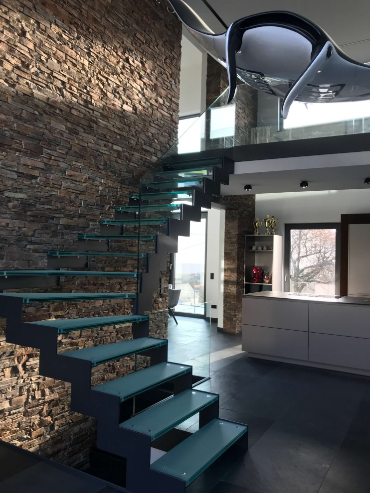Cette image montre un très grand escalier sans contremarche flottant minimaliste avec des marches en verre, un garde-corps en verre et un mur en parement de brique.