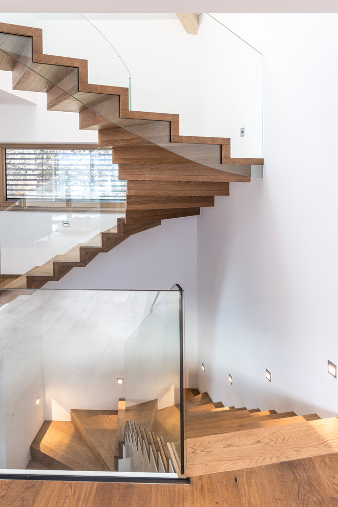 Modelo de escalera curva actual con escalones de madera, contrahuellas de madera y barandilla de vidrio