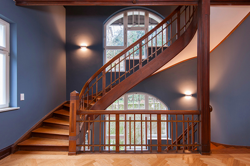 На фото: большая изогнутая деревянная лестница в классическом стиле с деревянными ступенями