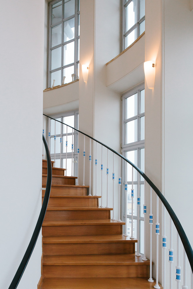 Пример оригинального дизайна: большая изогнутая деревянная лестница в стиле фьюжн с деревянными ступенями