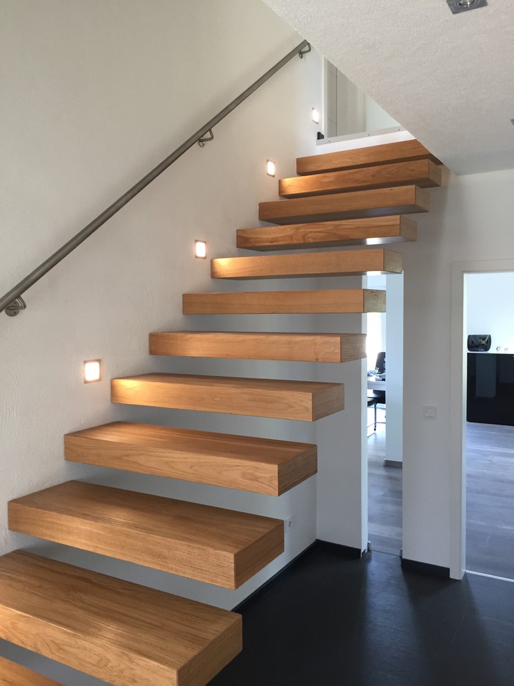 Diseño de escalera suspendida moderna grande sin contrahuella con escalones de madera y barandilla de metal