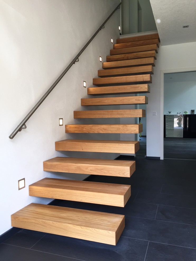 Imagen de escalera suspendida minimalista grande sin contrahuella con escalones de madera y barandilla de metal