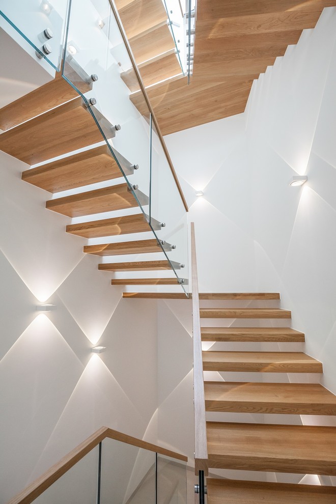 Réalisation d'un grand escalier courbe design avec des marches en bois peint et un garde-corps en verre.