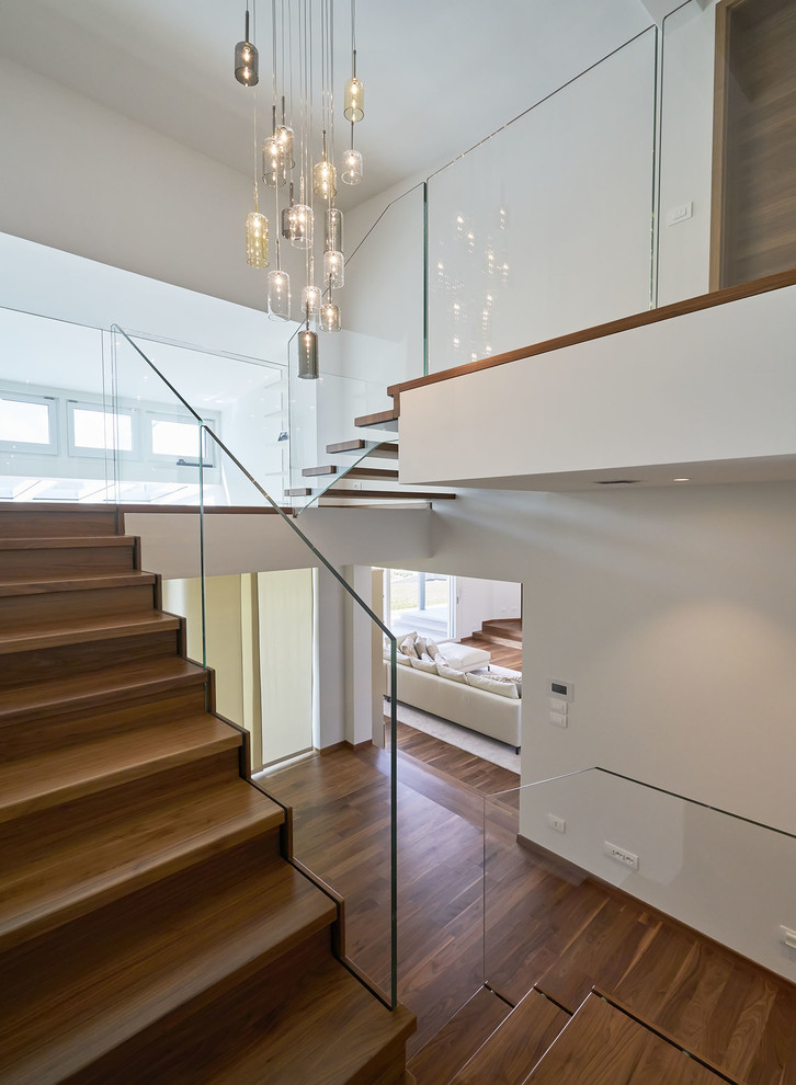 Photo of a medium sized modern painted wood u-shaped glass railing staircase in Munich with painted wood risers and feature lighting.