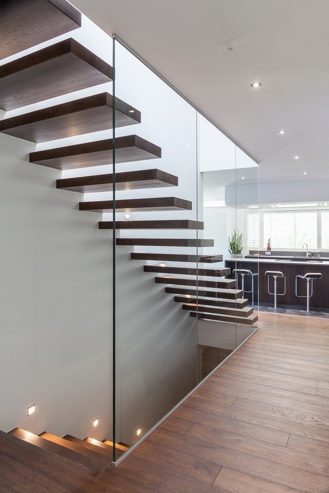 Ejemplo de escalera recta minimalista grande con escalones de madera pintada y barandilla de vidrio