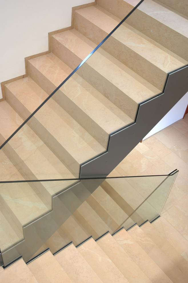 Photo of a large contemporary curved glass railing staircase in Other with limestone treads and limestone risers.