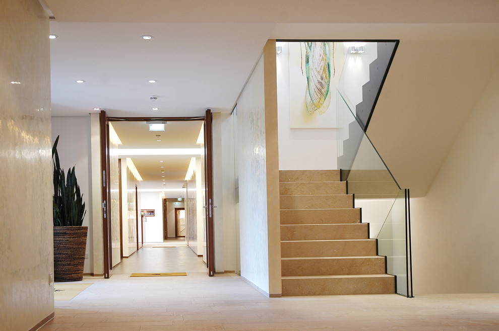 Пример оригинального дизайна: большая п-образная лестница в современном стиле с мраморными ступенями, подступенками из мрамора и стеклянными перилами
