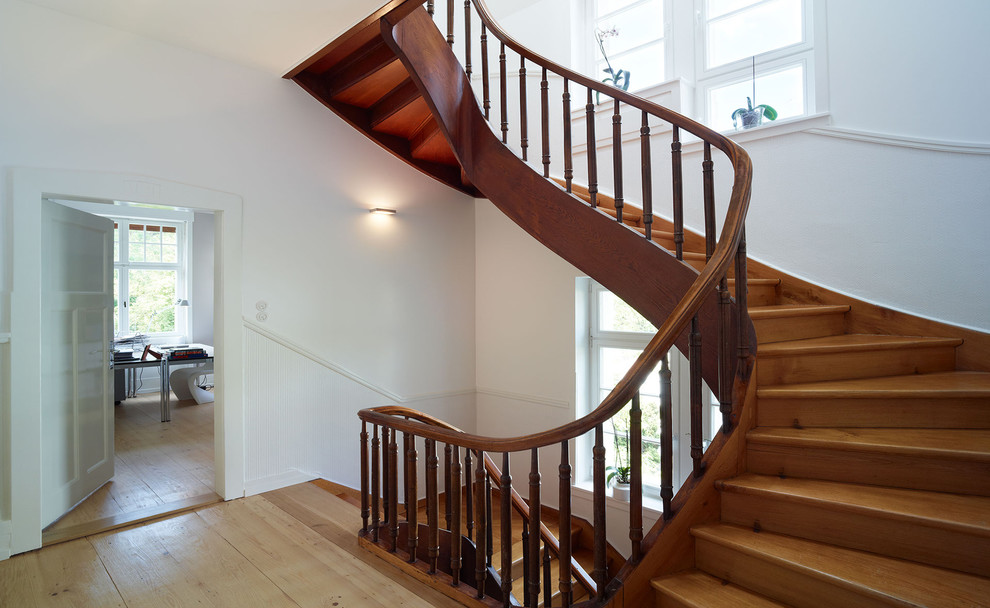 На фото: большая изогнутая деревянная лестница в классическом стиле с деревянными ступенями с