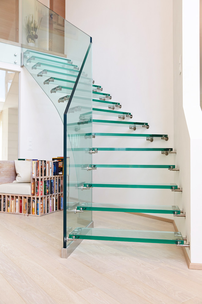 Cette image montre un escalier courbe design de taille moyenne avec des marches en verre et un garde-corps en verre.