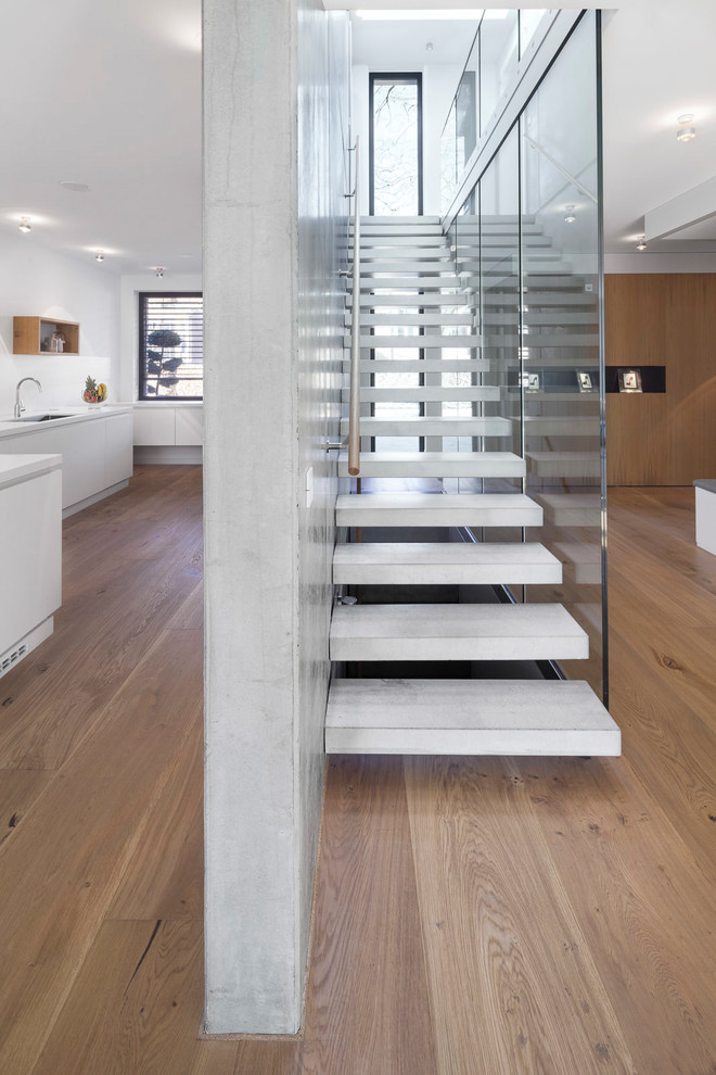 Medium sized modern concrete straight wood railing staircase in Hamburg with open risers.