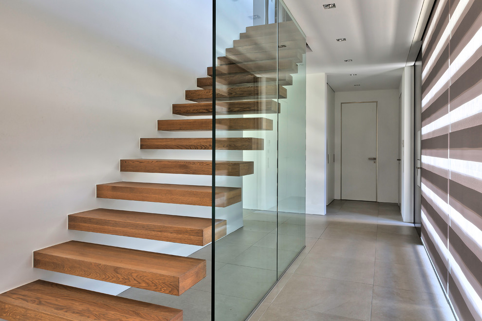 Пример оригинального дизайна: большая прямая лестница в стиле модернизм с деревянными ступенями без подступенок