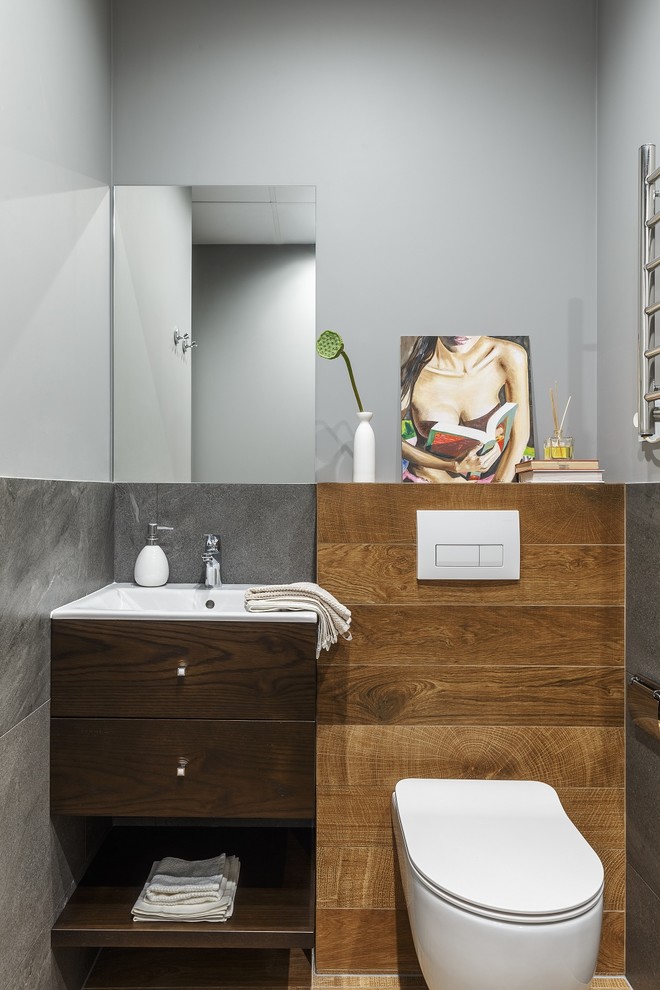 На фото: туалет в современном стиле с плоскими фасадами, темными деревянными фасадами, раздельным унитазом, серой плиткой и серыми стенами