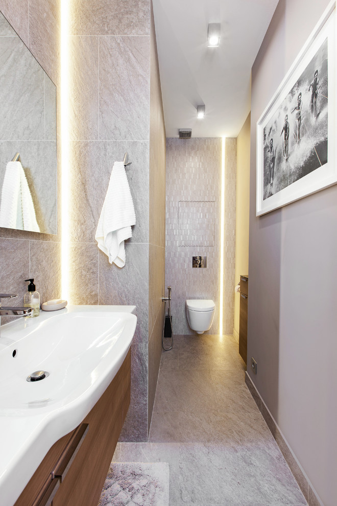 Cette image montre un WC suspendu design en bois brun de taille moyenne avec un placard à porte plane, un carrelage gris, des carreaux de porcelaine, un mur gris, un sol en carrelage de porcelaine, un sol gris et un lavabo intégré.