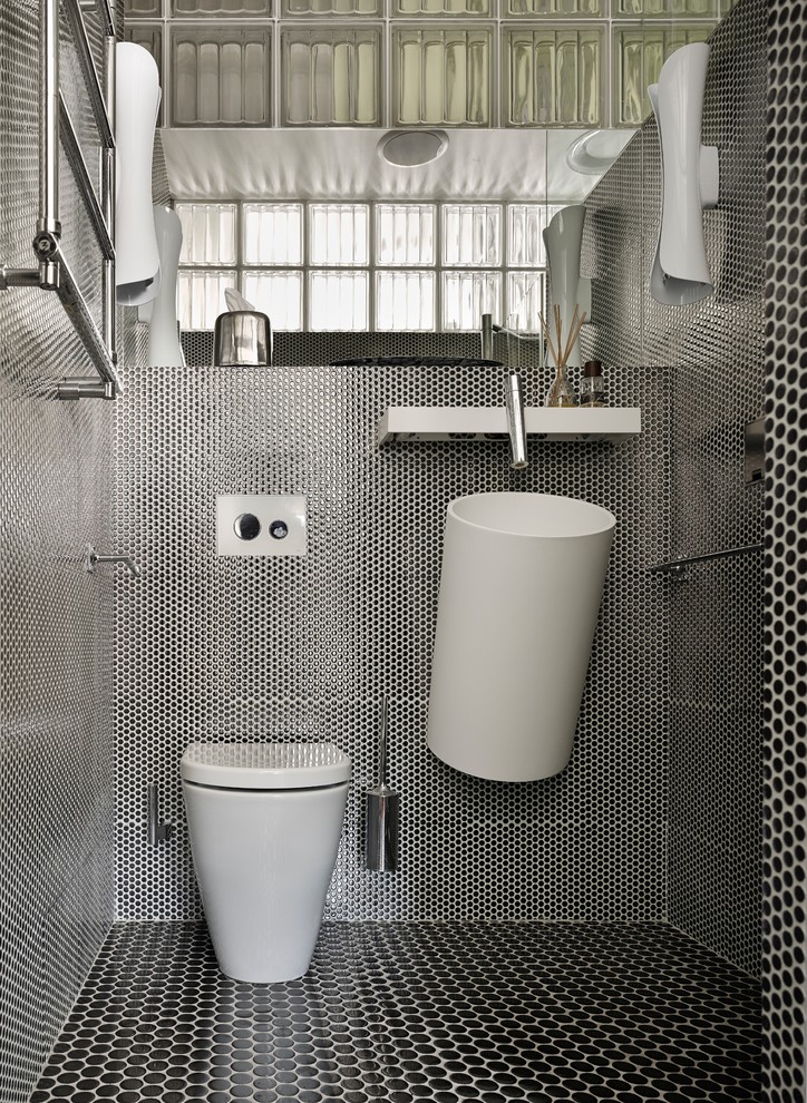 Inredning av ett modernt toalett, med svart och vit kakel, ett väggmonterat handfat, svart golv, en toalettstol med separat cisternkåpa, mosaik och mosaikgolv