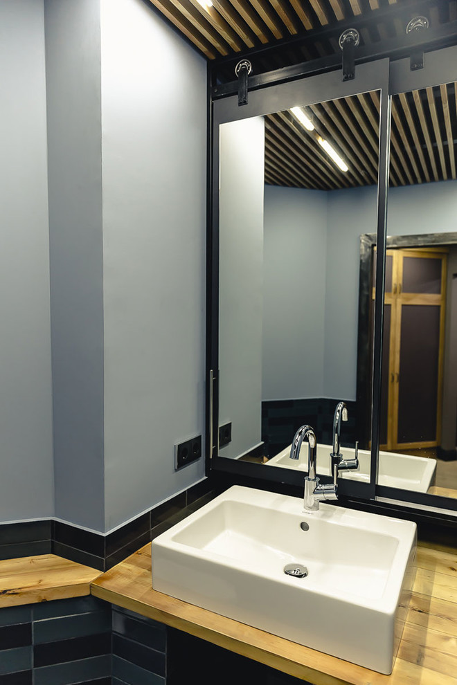 Inspiration för mellanstora industriella gult toaletter, med en vägghängd toalettstol, blå kakel, keramikplattor, blå väggar, klinkergolv i keramik, ett nedsänkt handfat, träbänkskiva och orange golv