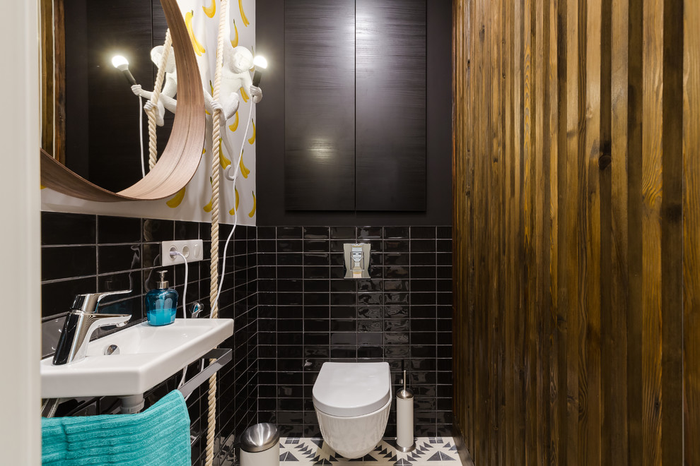 Inredning av ett modernt litet toalett, med en vägghängd toalettstol, svart kakel, vita väggar, cementgolv, flerfärgat golv, keramikplattor och ett väggmonterat handfat