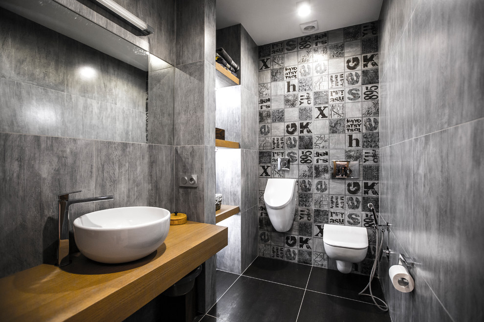 Ejemplo de aseo contemporáneo con urinario, baldosas y/o azulejos grises, lavabo sobreencimera, encimera de madera y suelo negro