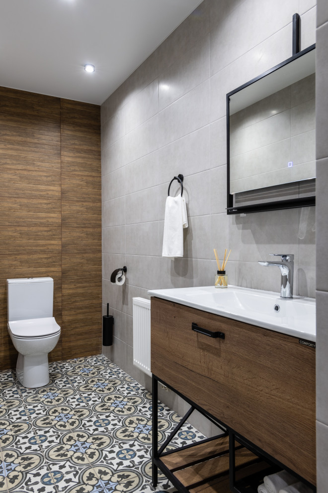Modern inredning av ett mellanstort vit vitt toalett, med släta luckor, skåp i mellenmörkt trä, en toalettstol med separat cisternkåpa, grå kakel, keramikplattor, grå väggar, klinkergolv i porslin, ett nedsänkt handfat, bänkskiva i akrylsten och grått golv
