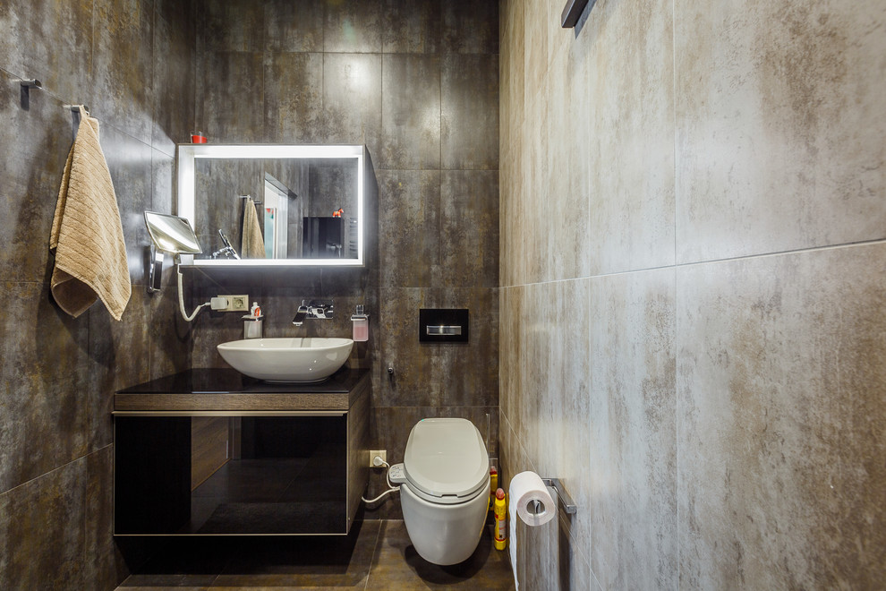サンクトペテルブルクにある小さなコンテンポラリースタイルのおしゃれなトイレ・洗面所 (フラットパネル扉のキャビネット、黒いキャビネット、壁掛け式トイレ、ガラスの洗面台、ベッセル式洗面器) の写真
