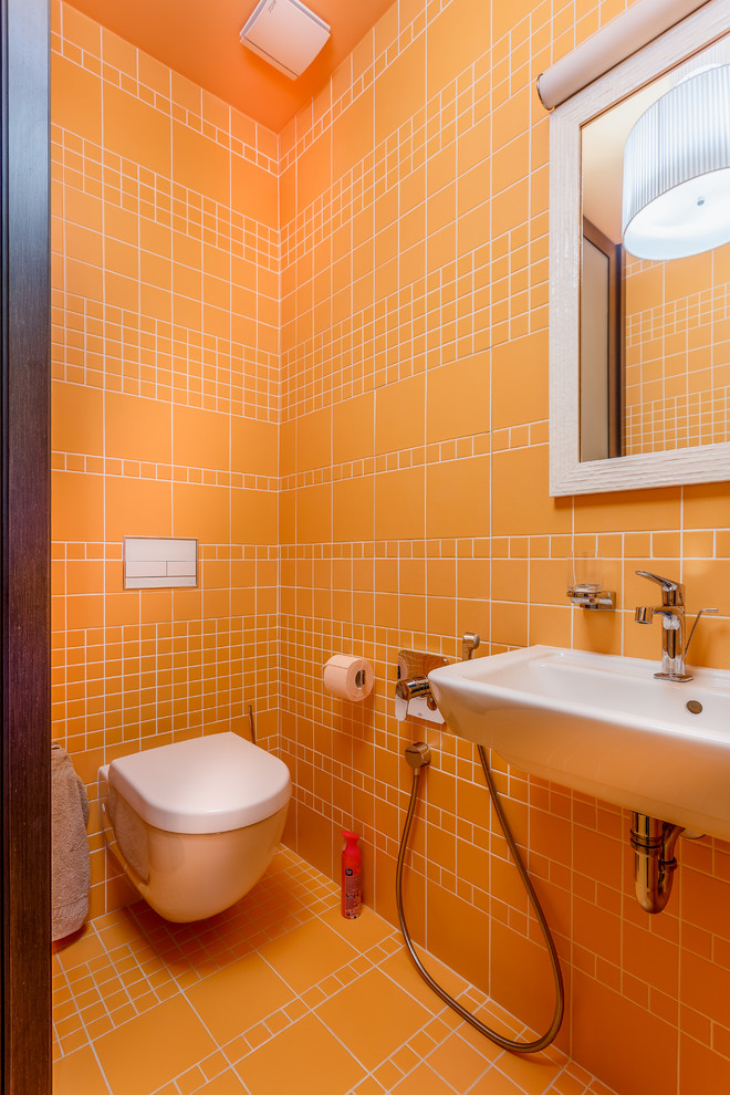 モスクワにあるコンテンポラリースタイルのおしゃれなトイレ・洗面所 (壁掛け式トイレ、オレンジのタイル、壁付け型シンク、オレンジの床) の写真