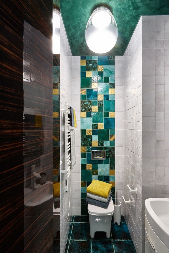 Inredning av ett modernt toalett, med vita skåp, en toalettstol med separat cisternkåpa, vit kakel, grön kakel, grå kakel, ett nedsänkt handfat och blått golv