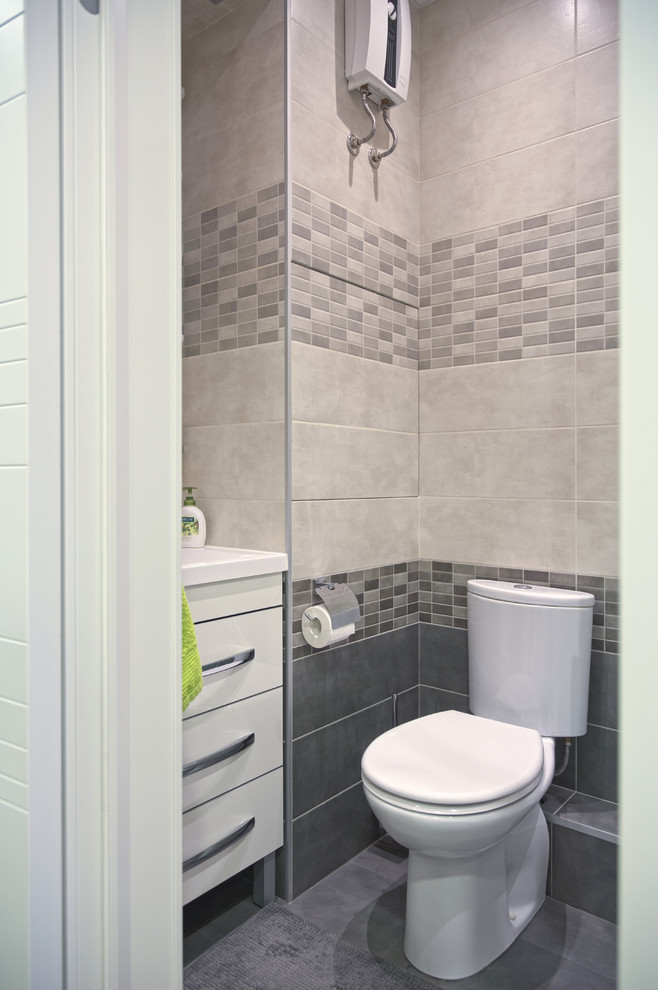 Idéer för små funkis toaletter, med släta luckor, vita skåp, en toalettstol med hel cisternkåpa, grå kakel, porslinskakel, grå väggar, klinkergolv i porslin, ett väggmonterat handfat och grått golv
